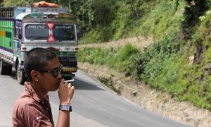 A man smokes on the side of the road as a bus passes in Nepal.