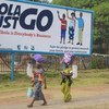 Deux femmes à Monrovia, au Libéria, marchent devant un panneau d'affichage, qui dit "En finir avec Ebola. Mettre fin à Ebola est l'affaire de tous". Photo : MINUL/Emmanuel Tobey