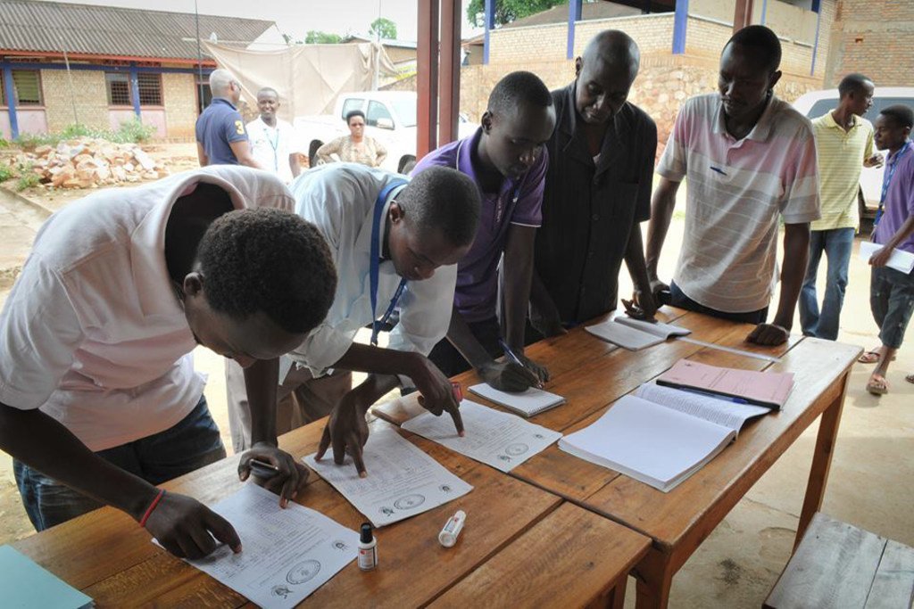 Au Burundi, les hommes s'inscrivent sur les listes électorales en remplissant des formulaires sur une table en bois pendant les élections.