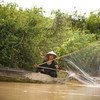 A woman casting a fishing net from a boat on the Tonle Sap River, Cambodia.