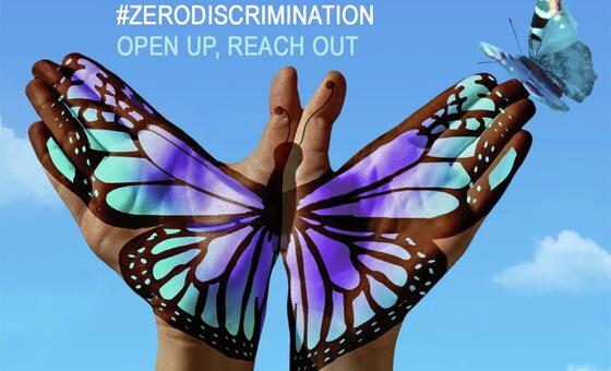 Mikono miwili iliyopakwa rangi na mabawa ya vipepeo, ikifikia chini ya anga ya bluu na kipepeo halisi akiruka karibu. Ufafanuzi wa maandishi unasema '#ZERODISCRIMINATION OPEN UP, REACH OUT'.