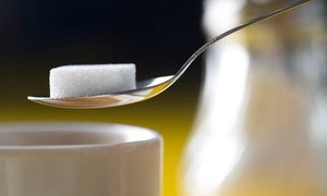 Um cubo de açúcar numa colher pairando sobre uma xícara de café.