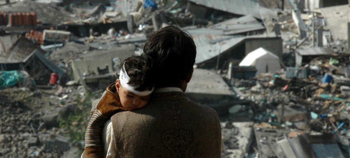 A father holds his injured child as he surveys the damage to the devastated city of Balakot, Pakistan, following an earthquake in 2005.