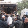 Une foule d'hommes se rassemble autour d'un camion et d'une camionnette de l'UNRWA tandis que des fournitures humanitaires sont déchargées au Moyen-Orient.