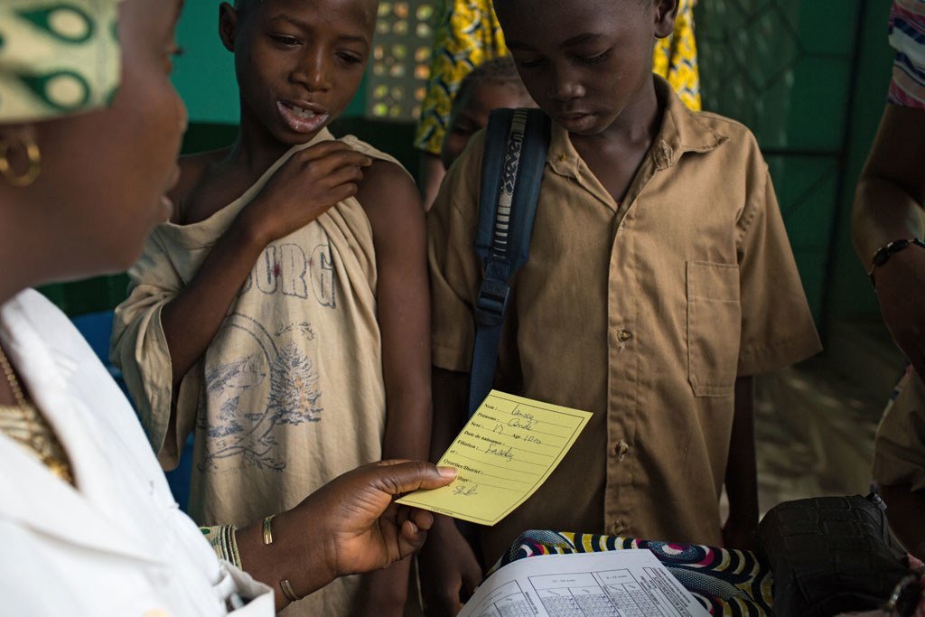 Une infirmière donne aux enfants leur carte de vaccination après avoir reçu la vaccination contre la rougeole et la poliomyélite, ainsi qu'un supplément de vitamine A au Centre de santé de Madina à Guéckédou, en Guinée.