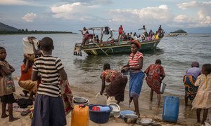 Women wash their cookware as a boat carring Burundian refugees approaches the shore at Mboko, a Congolese fishing village on Lake Tanganyika.