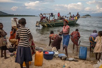 Women wash their cookware as a boat carring Burundian refugees approaches the shore at Mboko, a Congolese fishing village on Lake Tanganyika.