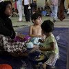 A rescued boat woman and her two children eat some welcome food at a centre in Kuala Cangkoi, Indonesia.