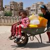 A girl pushes two younger children  in a wheelbarrow that also bears several jerrycans in Sana’a, the capital of Yemen.