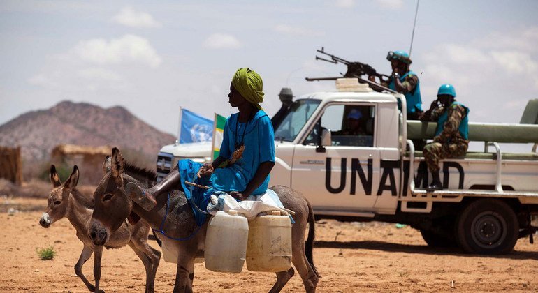 A woman rides a donkey loaded with water jerry cans, while Tanzanian troops with the Joint UN-African Union mission in Sudan’s Darfur region (UNAMID) conduct a routine patrol in the camp for internally displaced persons in Khor Abeche. (30 June 2014) 