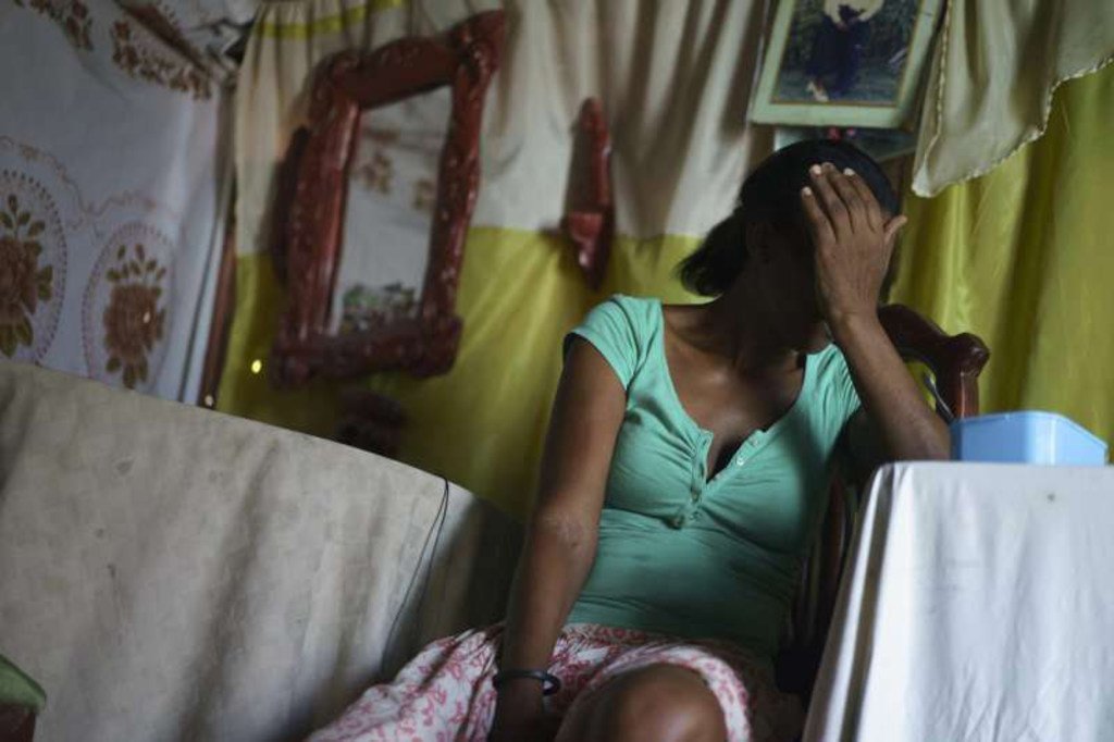 Una mujer está sentada en el interior de una casa, cubriéndose el rostro con la mano.