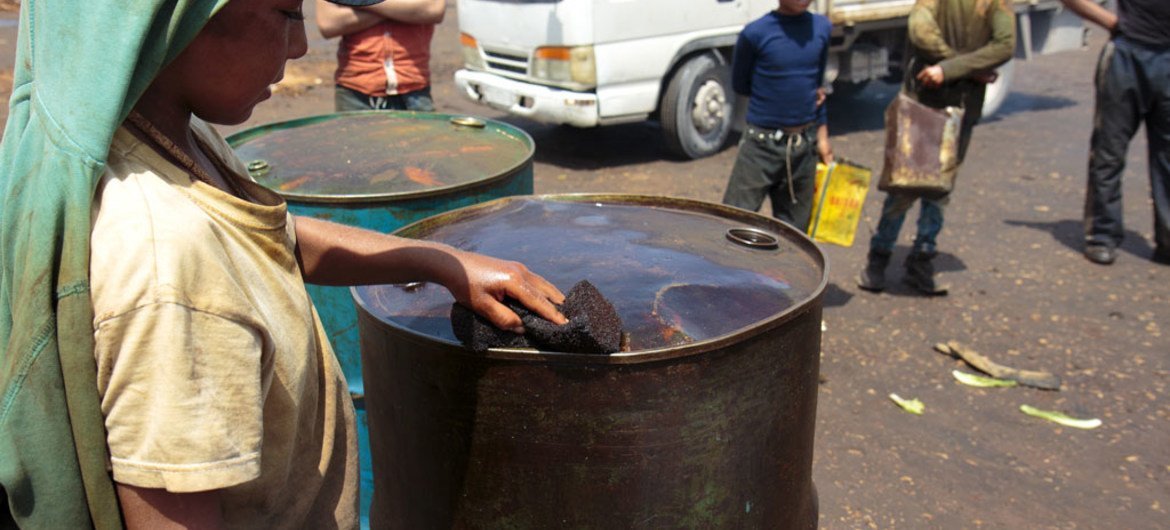 A boy in northern Syria uses a sponge to collect spilled fuel from an oil drum.
