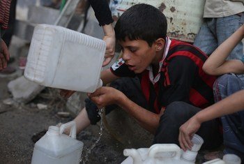 A boy drinks the remaining water in his jerrycan while waiting with other children in a queue for safe water, in the town of Douma. UNICEF/NYHQ2014-1125/Khabieh