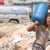 في المخيم تشرين للنازحين في حلب بسوريا، صبي يحمل وعاء ماء من خزان مياه بنته أوكسفام بدعم من اليونيسيف. صورة اليونيسيف / رزان رشيدي