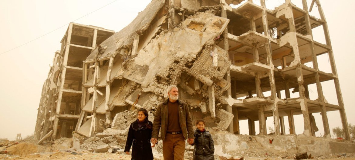 A man holds the hands of his granddaughters near the remnants of the residential towers where the girls used to live, in the city of Beit Lahia, in the northern Gaza Strip.