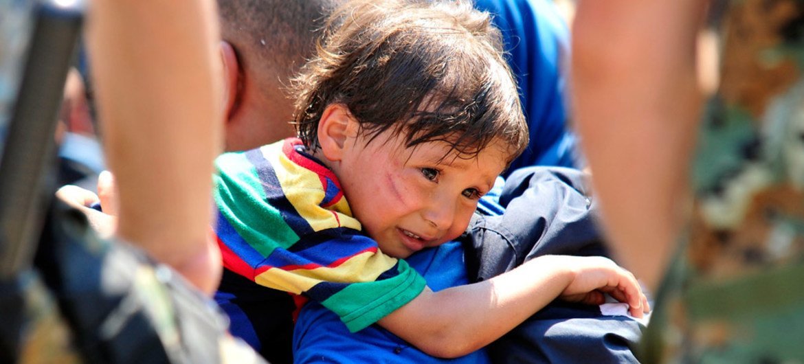 On 26 August 2015, a distressed child rests over the shoulder of the man carrying him, in the town of Gevgelija, on the border with Greece and the former Yugoslav Republic of Macedonia.