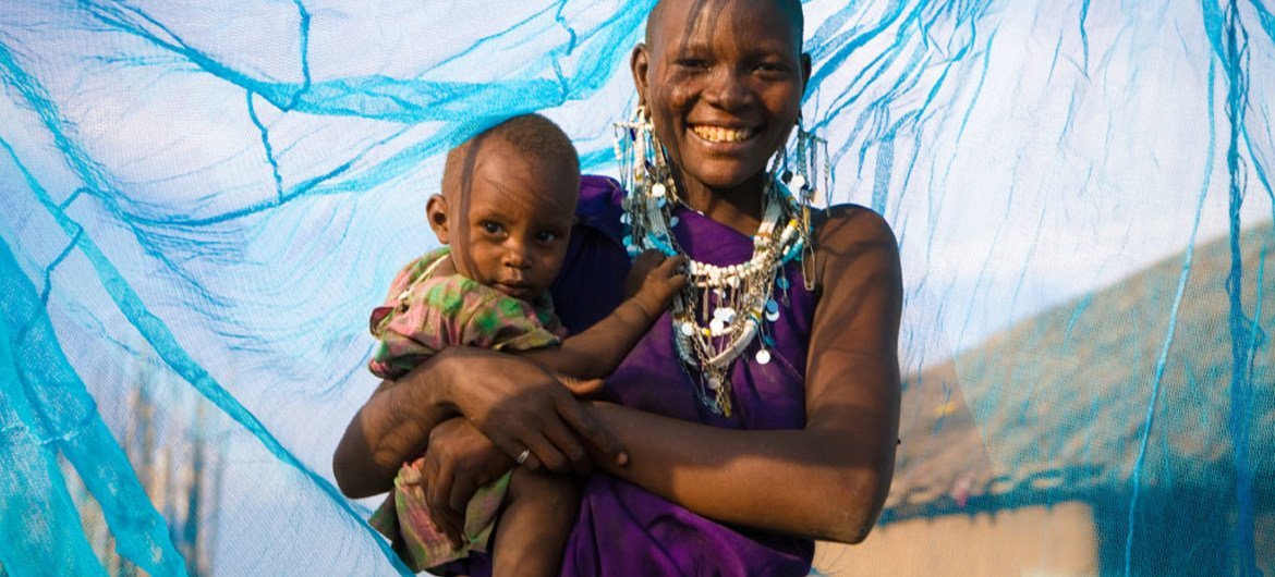 一位面带微笑的母亲抱着自己的孩子在防虐蚊帐里。儿基会图片/Hallahan