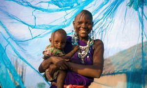 A smiling mother stands holding her young boy beneath an insecticide-treated net, in Arusha, Tanzania.
