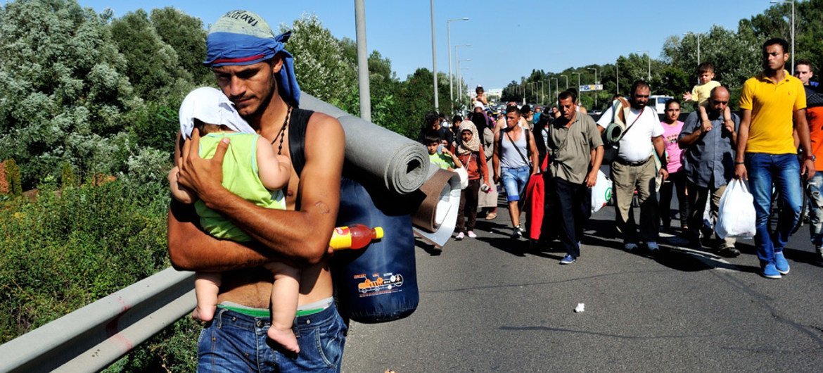 Un Syrien porte un bébé alors qu'il marche avec d'autres réfugiés en Hongrie en direction de l'Autriche. Photo HCR/Mark Henley