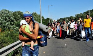 Syrian man carrying a baby along the highway with other refugees, several kilometres after leaving Budapest, Hungary, heading in the direction of Vienna, Austria.