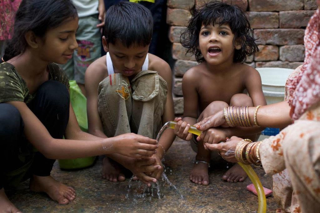 Trois enfants se lavant les mains avec de l'eau s'échappant d'un tuyau d'arrosage en Inde.