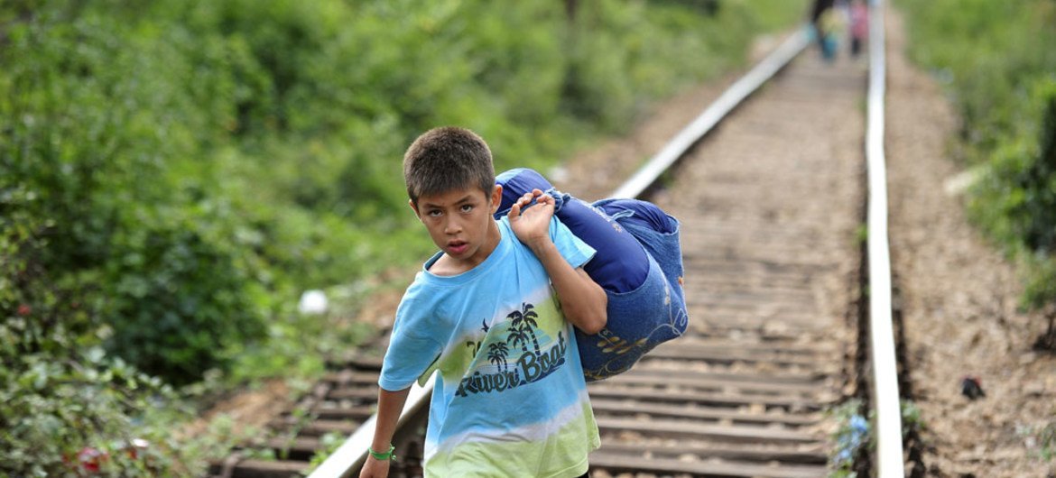 A boy carrying his belongings in a large cloth bag over his shoulder is among people walking on railway tracks to cross from the Former Yugoslav Republic of Macedonia into Serbia.