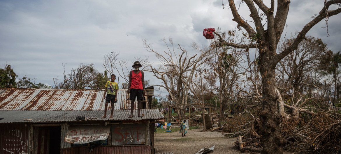 A child and an elderly man stand on the roof of a building damaged when Cyclone Pam hit Vanuatu in March 2015.