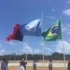 UN, Brazil, and Afghanistan flags flying at a ceremony with UN peacekeepers and personnel under a clear blue sky.
