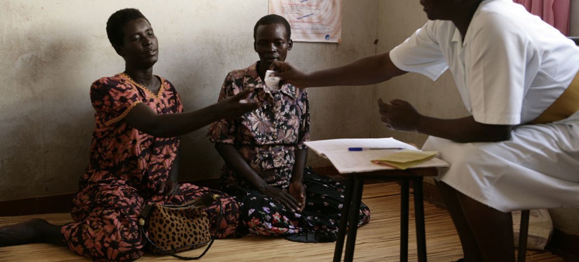 Deux femmes séropositives en Ouganda sont assises sur le sol, tandis qu'une infirmière leur donne des médicaments antirétroviraux. Photo : UNICEF / Shehzad Noorani