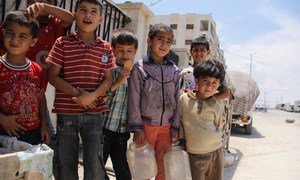 Boys, some carrying plastic containers for water, stand on a dusty street in the Tishreen camp for displaced persons in Aleppo, Syria.