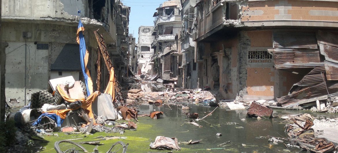 Destroyed buildings line a street – which is flooded with algae-covered, debris-filled water – in the Old City area of Homs, the capital of Homs Governorate, Syria.