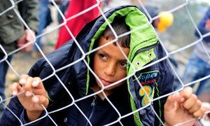 A boy clutches and looks through a chain-link fence, on a rainy day near the Former Yugoslav Republic of Macedonia town of Gevgelija, on the border with Greece. September 2015