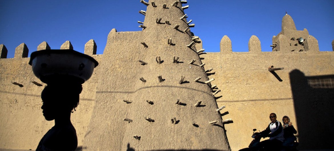 Residents of Timbuktu pass by Djingareyber Mosque, one of the historical architectural structures  along with Sankore Mosque, Sidi Yahia Mosque and sixteen mausoleums and holy public places  which together earned Timbuktu the designation of World Heritage