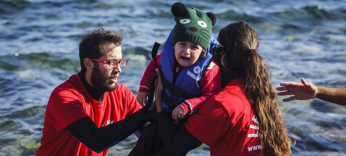 Voluntarios griegos ayudan a un niño pequeño a desembarcar al llegar a las costas de la isla griega de Lesbos, tras cruzar el mar Egeo desde Turquía. Foto: ACNUR/Achilleas Zavallis