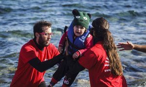 Greek volunteer life-guards help a young child out of a boat that reached the shores of Lesbos, having crossed the Aegean sea from Turkey.