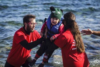 Greek volunteer life-guards help a young child out of a boat that reached the shores of Lesbos, having crossed the Aegean sea from Turkey.