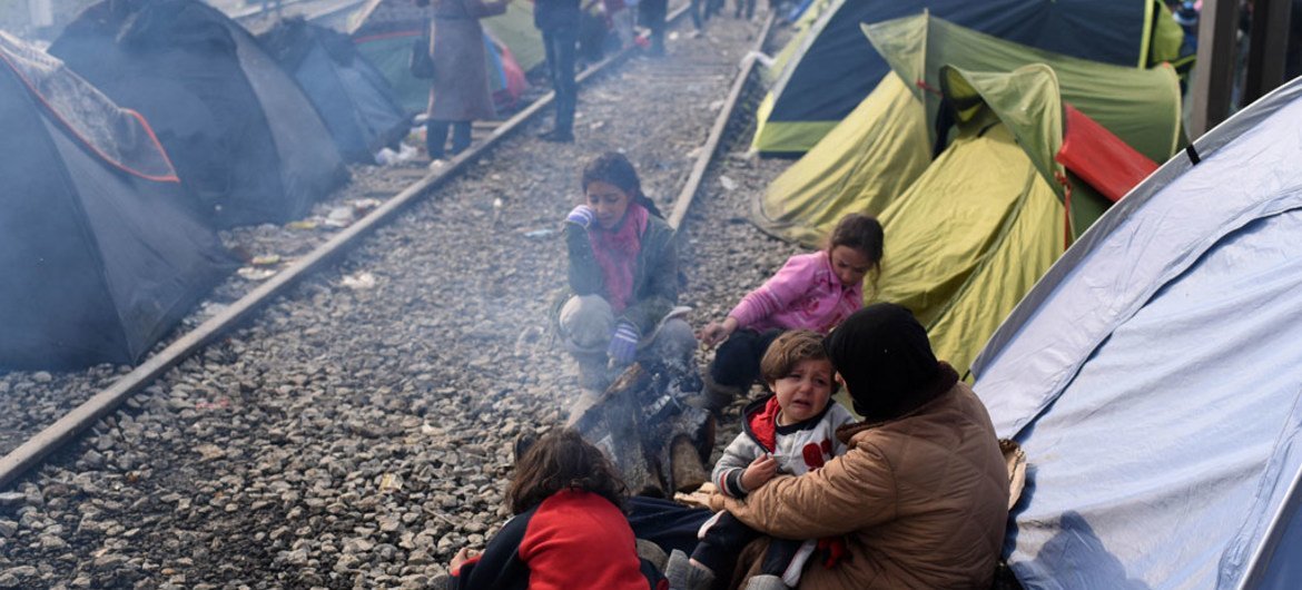 أم تحمل طفلها وهو يبكي، بينما تجلس بناتها الثلاث الأخرى أمام النار خارج خيمة مؤقتة في إدومني باليونان. UNICEF/Tomislav Georgiev