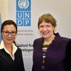 Two women standing in front of a UNDP banner and a flag.