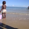 A small boy holds onto a bucket as he wades on the beach in Anosikely, a neighbourhood in Morondava, Madagascar. Behind him, women use nets to fish.