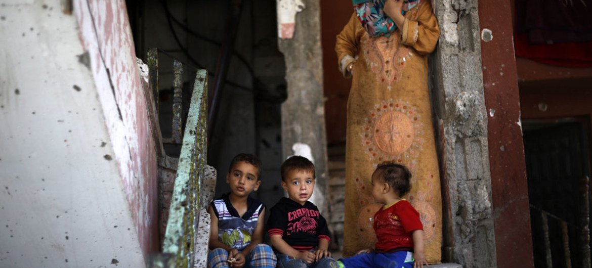 Toddlers sit on the top step and their grandmother stands on a landing, inside their partially destroyed home in the Shejaiya neighbourhood of Gaza City. UNICEF/UNI188296/El Baba