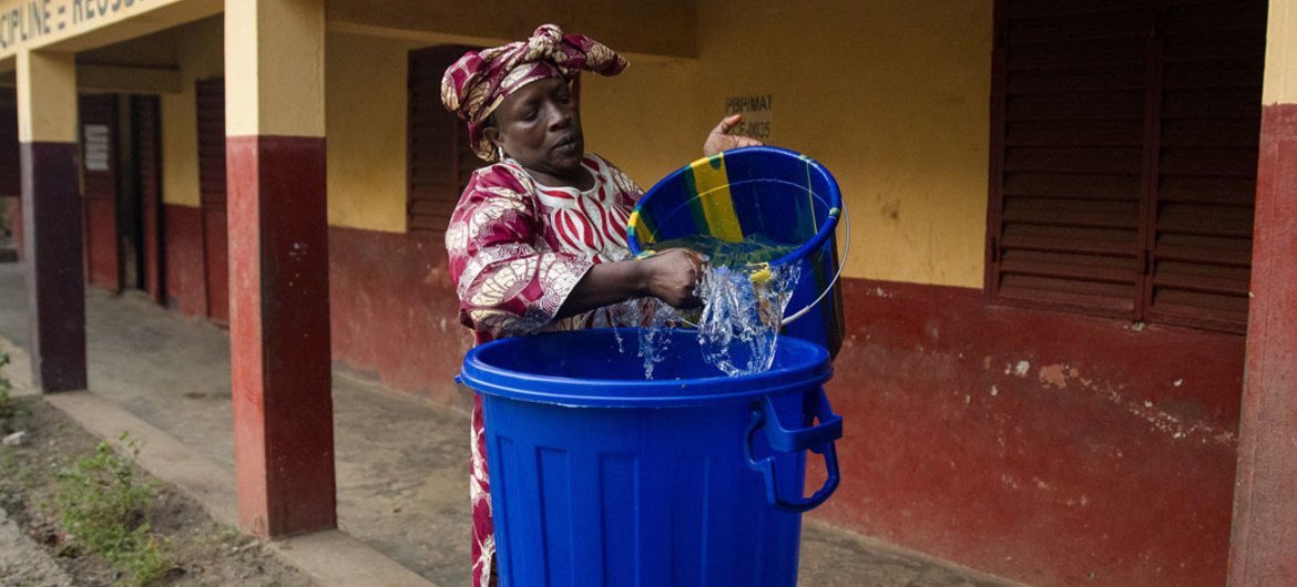 A teacher is preparing a bucket with water to use for hand washing. After being kept closed for three months due to the Ebola outbreak, schools across Guinea reopened on 19 January 2015.