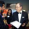 UN Secretary-General Ban Ki-moon presents a certificate to a man in a blazer at an indoor event.
