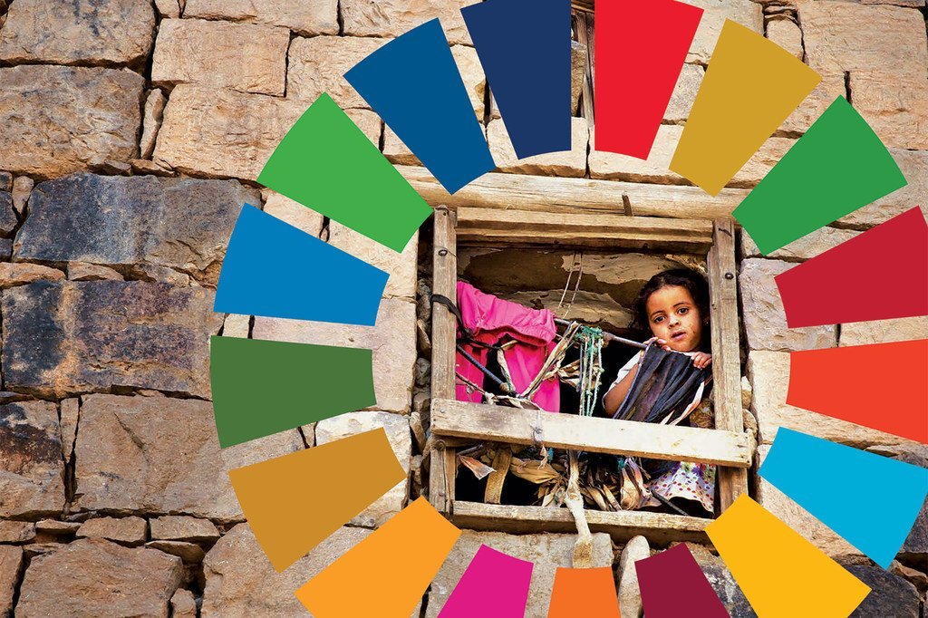 فتاة صغيرة تنظر من نافذة في منزل حجري، محاطة برسم ملون لشعار أهداف التنمية المستدامة.