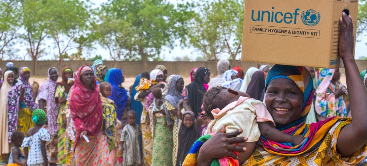 A woman carrying a baby smiles as she leaves a distribution site with a family hygiene and dignity kit, in the Dalori camp for internally displaced people, in the north-eastern Nigerian city of Maiduguri in Borno State.