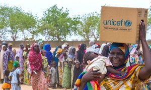 Une femme portant un bébé sourit alors qu'elle quitte un site de distribution avec un kit familial d'hygiène et de dignité, dans le camp pour déplacés internes de Dalori, situé dans la ville de Maiduguri, Etat de Borno (nord-est du Nigéria).