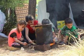 In the Syrian Arab Republic, an extended family takes shelter under a makeshift tent on the sidewalk after the latest wave of attacks.. The grandfather is wheelchair-bound. The children prepare a fire for cooking and hang out clothes to dry.