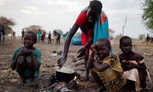 A woman cooks a meal outside in the open air with her three children where she is camping with her family the night before being able to register for a ration card  in Thanyang, South Sudan.