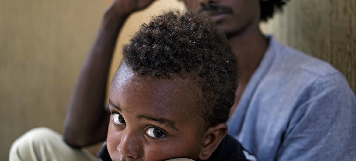 في ليبيا، مهاجر يحمل ابنه البالغ 30 شهرا، في زنزانة في مركز اعتقال  في الساحل الشمالي الغربي. اليونيسف / UNI187398 / رومنزي