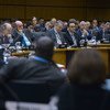 Delegates attend a formal meeting in a conference room, with nameplates for Canada, Brazil, and Germany visible.