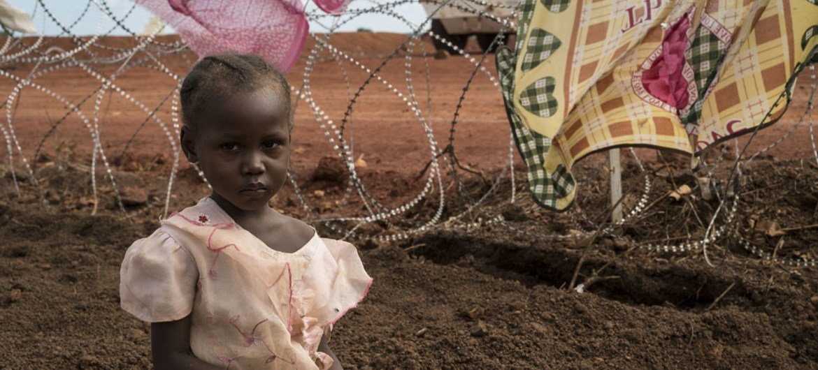 Niema, 3, sits while her mother washes clothes along the outer fence of the UN Protection of Civilians Site that houses over 30,000 displaced people in Wau, South Sudan.